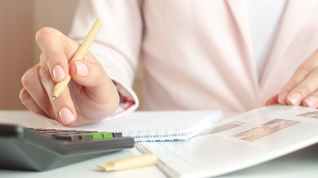 Cerca de la mano de la mujer con calculadora contando y tomando notas en el cuaderno.