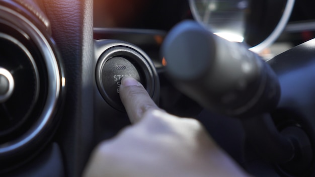 Cerca de la mano de la mujer, ella presiona la tecla de inicio en un automóvil moderno.