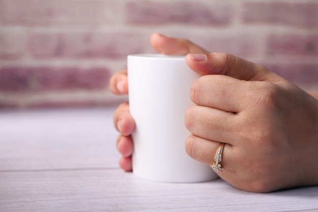 Cerca de la mano de la mujer sosteniendo la taza de café de color blanco.