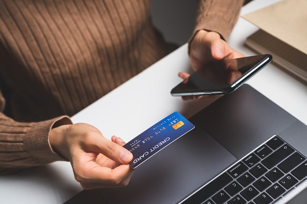 Cerca de la mano de la mujer con teléfono celular o móvil para comprar en línea o pagar con tarjeta de crédito. Concepto de compras en línea.