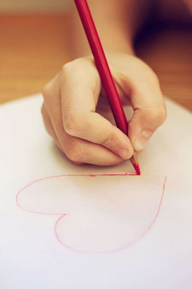 Foto cerca de la mano del niño dibujo corazón a lápiz