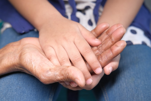 Cerca de la mano del niño sosteniendo la mano de mujeres mayores