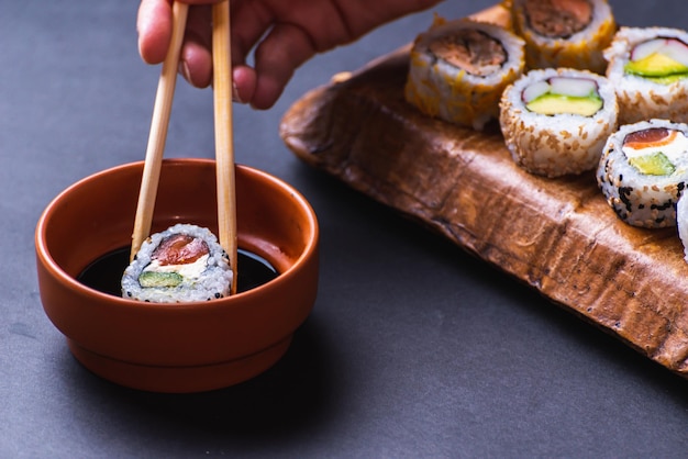 Cerca de la mano con palillos sumergiendo sushi en salsa de soja