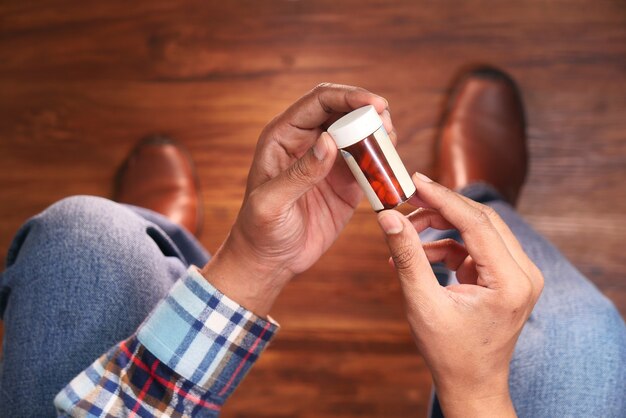 Cerca de la mano de la persona que sostiene el contenedor de pastillas.