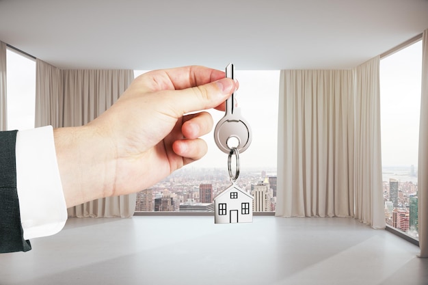 Foto cerca de la mano sosteniendo la llave con la cadena de la casa en el interior moderno con vista a la ciudad concepto de bienes raíces