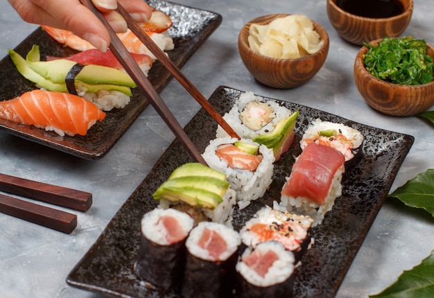 Cerca de la mano tomando rollo con palillos de un plato en la barra de sushi