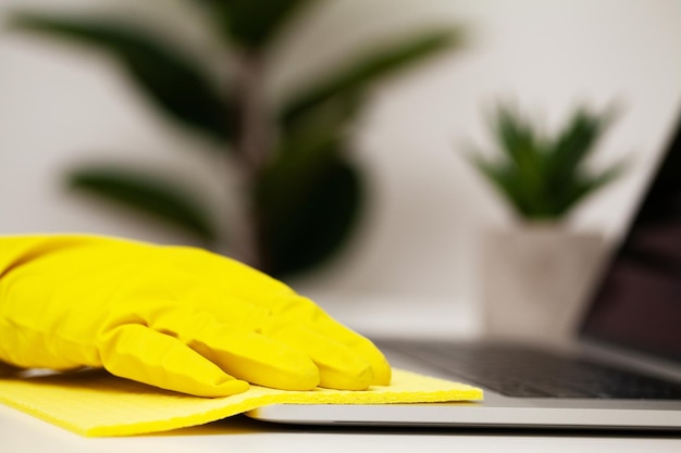 Cerca de la mano del trabajador limpiando el polvo en la oficina con guantes amarillos.