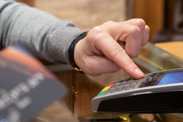 Cerca de la mano usando la máquina de deslizar la tarjeta de crédito para pagar. Mano con pase de tarjeta de crédito a través de terminal para pago en cafetería. Hombre ingresando el código de la tarjeta de crédito en la máquina deslizante.