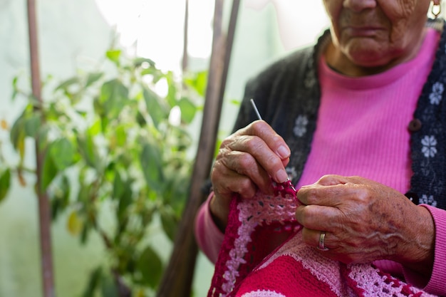 Cerca de las manos de la anciana tejiendo en casa