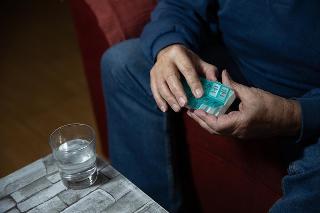 Cerca de las manos de un anciano tomando pastillas de su organizador de pastillas