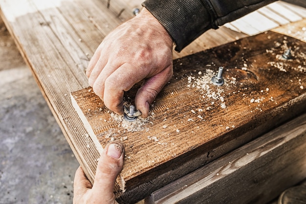 Cerca de manos atornillando un perno en una tabla de madera