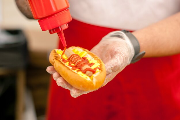 Cerca de las manos del chef de la calle agregando salsa de tomate en hot dog