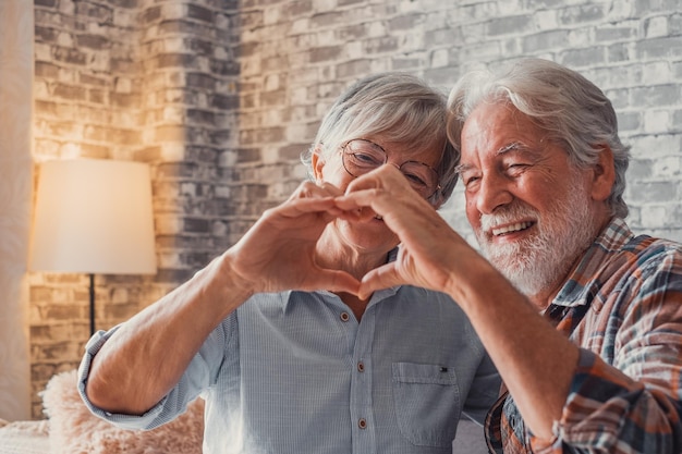 Cerca de las manos de dos abuelos maduros haciendo una forma de corazón con los dedos juntos sonriendo y divirtiéndose en la gente del amor