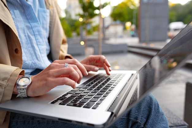 Cerca de manos femeninas escribiendo en el teclado de una computadora portátil sentada en la calle