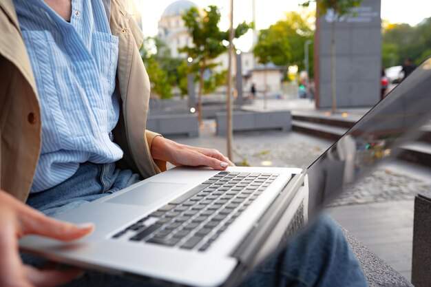 Foto cerca de manos femeninas escribiendo en el teclado de una computadora portátil sentada en la calle