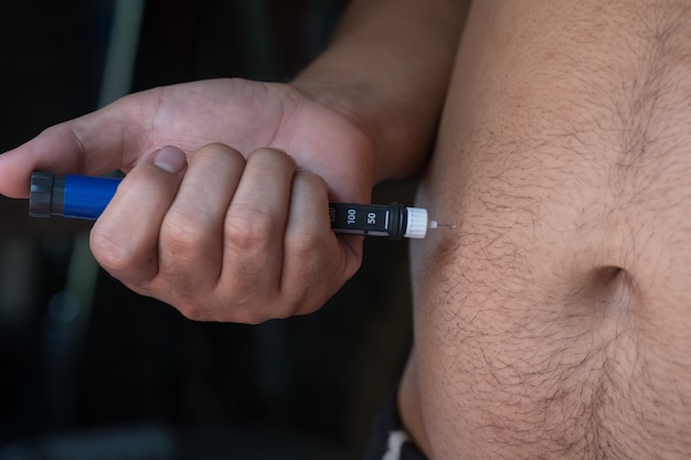 Foto cerca de las manos gordas del hombre que hacen la inyección con pluma de insulina
