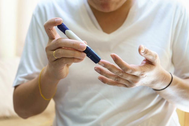 Cerca de las manos del hombre con una lanceta en el dedo para comprobar el nivel de azúcar en sangre con el medidor de glucosa. Uso como concepto de medicina, diabetes, glucemia, atención médica y personas.