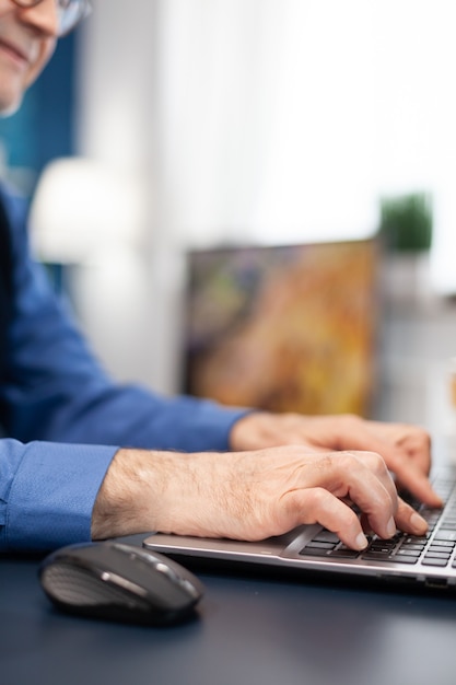 Cerca de las manos del hombre senior escribiendo en el teclado de la computadora portátil