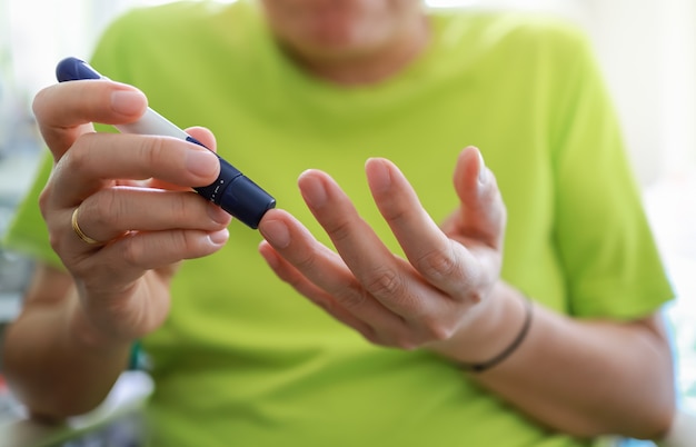 Cerca de las manos del hombre usando la lanceta en el dedo para verificar el nivel de azúcar en la sangre por medidor de glucosa en el dormitorio en la mañana. Uso como concepto de diabetes.