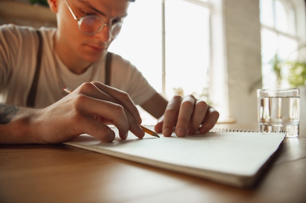 Cerca de manos masculinas escribiendo en un papel vacío sobre la mesa en casa