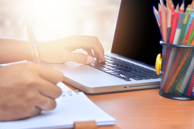 Cerca de manos masculinas usando la computadora portátil en el escritorio, tonificada con la luz del sol
