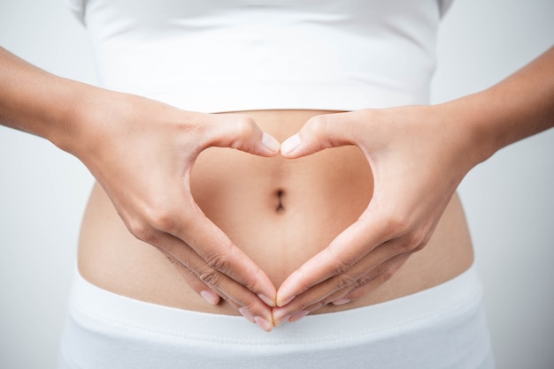 Foto cerca de las manos de la mujer hizo corazón en el vientre