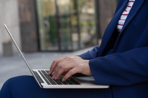 Cerca de las manos de una mujer de negocios usando una computadora portátil escribiendo trabajando en línea en el lugar de trabajo