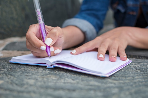 Foto cerca de las manos de una mujer que escribe en su diario personal.