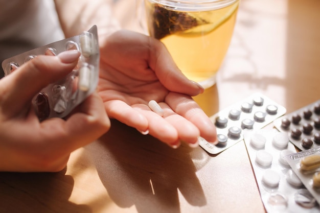 Cerca de las manos de la mujer sostienen pastillas Mano con pastillas y té negro con limón Inmunidad Vitaminas