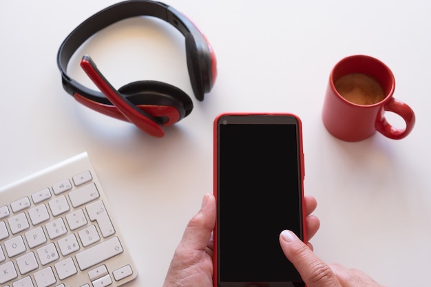 Cerca de las manos de la mujer mediante teléfono móvil. Escritorio blanco y accesorios rojos