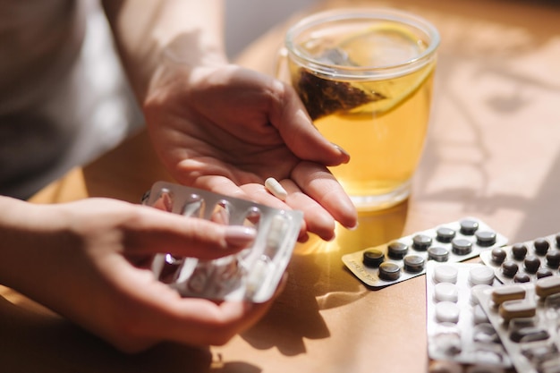 Cerca de las manos de las mujeres sostenga la mano de las pastillas con pastillas y té negro con vitaminas de inmunidad al limón