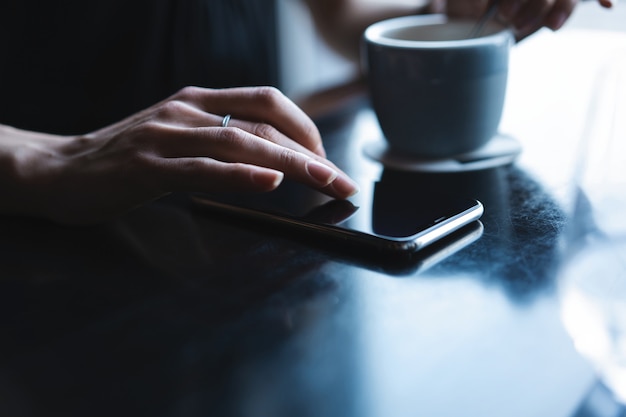 Cerca de las manos de las mujeres sosteniendo el teléfono inteligente, mujer mediante teléfono móvil durante la pausa para el café.