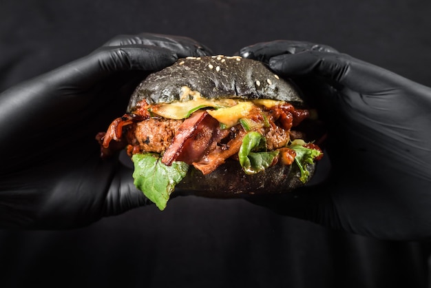 Cerca de manos sosteniendo hamburguesa jugosa negra