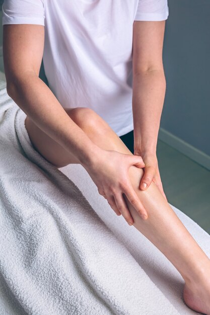 Cerca de las manos de la terapeuta femenina haciendo masaje de drenaje linfático en las piernas de la mujer en un centro clínico. Concepto de medicina, salud y belleza.