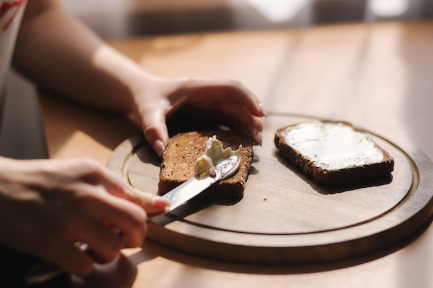 Cerca de mantequilla femenina el pan tostado de centeno con mantequilla vegana. Tostada de mantequilla de mujer en casa en