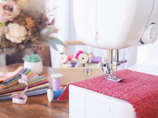 Cerca de la máquina de coser trabajando con tela roja coser accesorios en la mesa coser ropa nueva