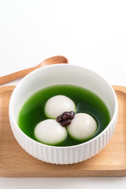 Cerca de matcha big tangyuan (tang yuan) con sopa de matcha dulce y pasta de frijoles rojos en un recipiente sobre fondo blanco de mesa para la comida del festival.