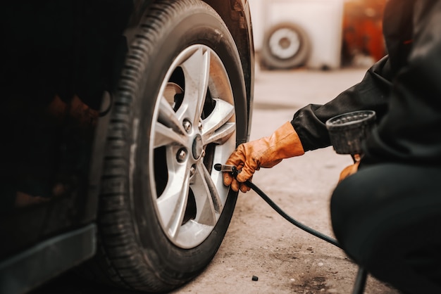 Cerca de mecánico de automóviles con bomba de neumáticos en el neumático de automóvil en el taller.