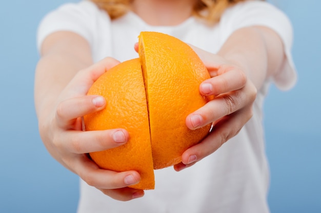 De cerca, media naranja en manos de niña aislada en azul