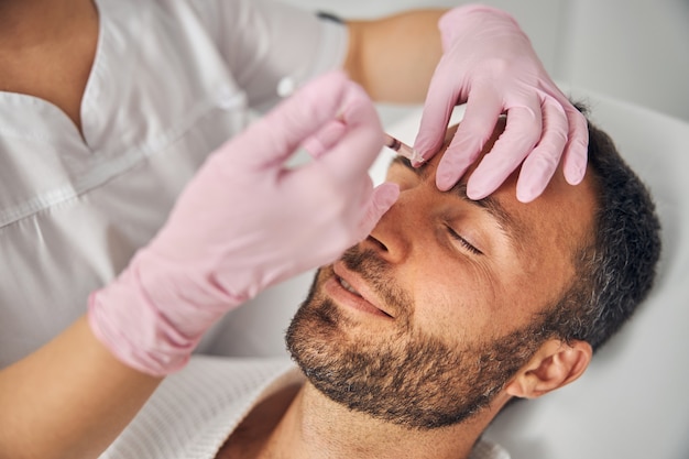 Cerca de médico cosmetólogo en guantes estériles haciendo inyección en la frente masculina