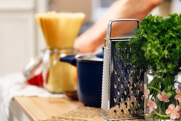 Cerca de la mesa de la cocina con la olla ralladora y espaguetis crudos