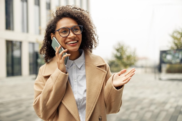 Cerca de una mujer afroamericana con gafas hablando por teléfono con amigos durante la caminata por la ciudad