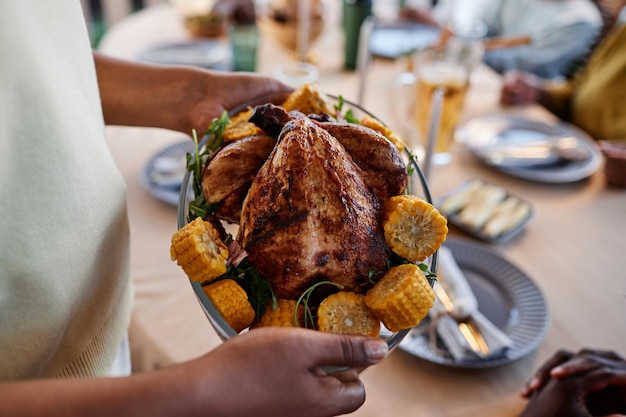 Cerca de una mujer afroamericana trayendo un plato de pollo casero a la mesa en una reunión familiar