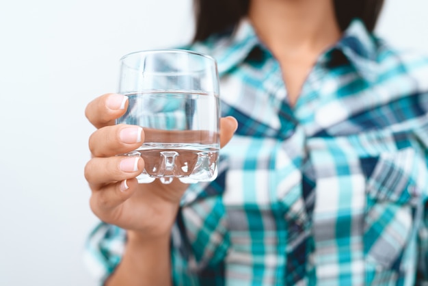 De cerca. Mujer en camisa a cuadros está sosteniendo un vaso con agua.