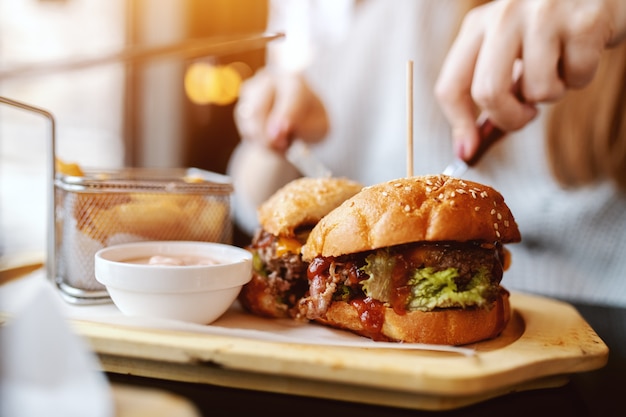 Cerca de mujer caucásica comiendo deliciosa hamburguesa mientras está sentado en el restaurante.