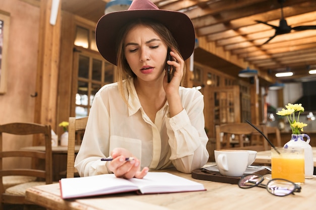 Cerca de una mujer confundida con sombrero sentado en la mesa de café