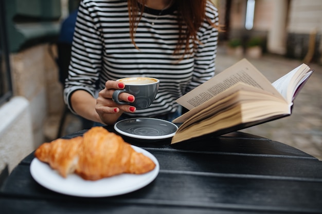 Cerca de la mujer disfrutando del café de la mañana con el libro en las manos en la terraza del café