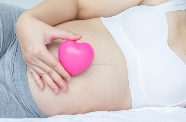 Foto cerca de una mujer embarazada feliz sosteniendo un corazón rojo de amor en su vientre concepto amoroso