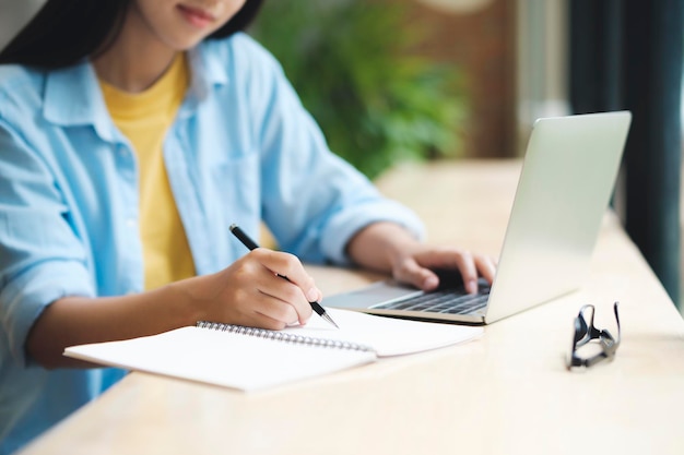 Cerca de una mujer estudiando leyendo un libro y tomando notas usando una laptop