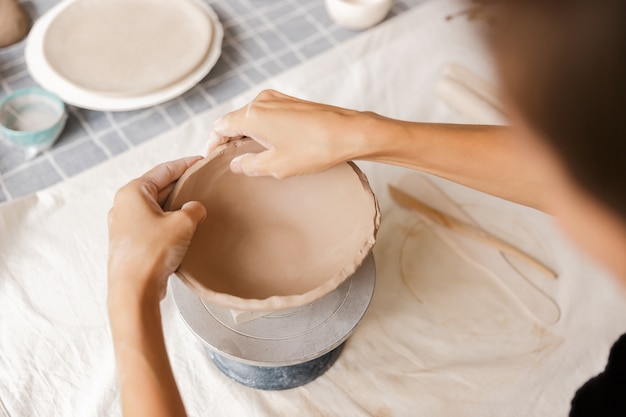 Foto cerca de una mujer haciendo vajillas de cerámica y alfarería en el taller, trabajando con arcilla